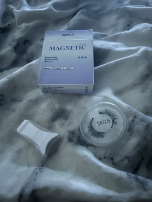 Magnetiska lösögonfransar M05 - Säljer ett par magnetiska lösögonfransar i modellen M05 från open. Fransarna är svarta och kommer i ett runt plastetui. Förpackningen är lila och vit och det medföljer ett verktyg för enkel applicering. Perfekt för dig som vill ha fylligare fransar utan lim.