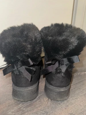 Svarta boots med fuskpäls och rosetter - Fina svarta boots med fluffig fuskpäls runt kanten och söta rosetter bak
