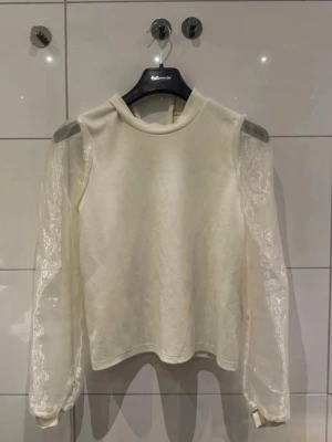 Vit topp med transparenta ärmar Pieces - Säljer en vit topp från Pieces i storlek M. Toppen har höghalsad krage och långa, transparenta puffärmar i mesh som ger en unik look. Kroppen är i mjuk bomullsmix och ärmarna har subtila volangdetaljer vid handlederna. Perfekt för dig som vill sticka ut lite extra.