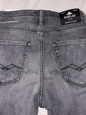 Replay grå jeans straight fit - Säljer ett par gråa Replay jeans med klassisk femficksdesign och snygga detaljer på bakfickorna. Jeansen har en rak passform och är tillverkade i mjukt denimtyg. Perfekta för dig som gillar stilrena och tidlösa jeans. , Använda 2 gånger så helt nytt skick 