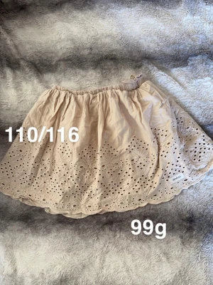 Beige kjol med broderade detaljer - Supersöt beige kjol från newbie med elastisk midja och broderade blommönster samt hålbroderier längs kanten. Kjolen har en luftig och lätt form, perfekt för varma dagar och ger en romantisk vibe till outfiten.🌸 Fint använt skick. Storlekslapp borta men står 110/116 på tvättrådslappen 