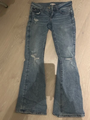 Blå bootcut jeans med slitningar - Säljer ett par blå bootcut jeans med snygga slitningar på låren och knäna. ❤️