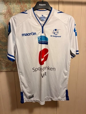 FK Haugesund Macron 2015 shirt, storlek M - Gott skick.  #fkhaugesund #norge #obos-ligæn #bamberg #kristiansen #gytkjaer  Vit FK Haugesund matchtröja med klubbens och sponsorers logotyper tryckta på framsidan. Tröjan har blå detaljer vid kragen och ärmarna.