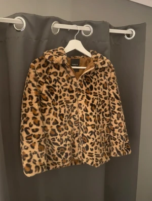 Leopardmönstrad pälsjacka från Name It - Säljer en fluffig pälsjacka från Name It med leopardmönster. Jackan har dragkedja framtill, huva och är helfodrad i brunt tyg. Perfekt för dig som vill sticka ut med en cool och trendig look. Jackan är mjuk och har lång ärm.