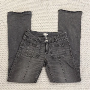 Grå jeans med utsvängda ben från Gina Tricot - Snygga grå jeans från Gina Tricot med utsvängda ben och coola framfickor. Jeansen har dubbla knappar i midjan, bälteshällor och klassiska bakfickor. Perfekta för dig som gillar en avslappnad men trendig look.