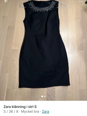 Svart kort klänning från Zara - Säljer en svart, figurnära kort klänning från Zara med snygga pärldetaljer runt halsringningen. Klänningen är ärmlös och har en klassisk, stilren look som passar perfekt när du vill känna dig extra snygg.