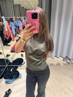 Olivgrön ribbad topp med kort ärm - Säljer en stilren olivgrön topp med ribbade detaljer i nederkant och ärmslut. Toppen har korta ärmar och en klassisk rund halsringning. Materialet känns mjukt och stretchigt, perfekt för en clean och enkel look.