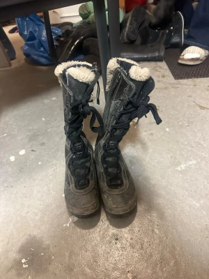 Svarta vinterboots från Merrell - TVÄTTAS INNAN SKICKNING!!!!!Säljer ett par svarta vinterboots från Merrell med snörning och dragkedja på sidan. Bootsens insida är fodrad med mjuk beige pälsimitation för extra värme. Yttermaterialet är mocka och syntet, perfekt för kalla dagar. Höga skaft och robust sula. 