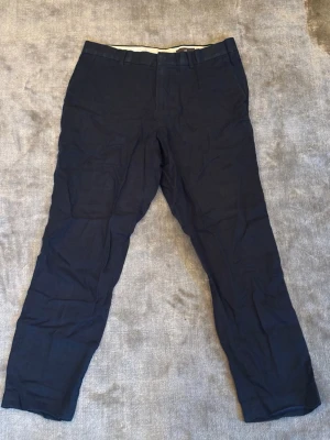 Mörkblå linnebyxor från H&M - Snygga mörkblå linnebyxor från H&M i straight fit-modell. Byxorna har klassiska fickor fram och bak, bälteshällor och stängs med dragkedja och knapp. Perfekta för en stilren och avslappnad look till sommaren