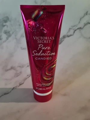 Victoria's Secret Pure Seduction Candied - En lyxig body lotion från Victoria's Secret i serien Pure Seduction Candied. Tuben är metallicrosa med godisdetaljer och rymmer 236 ml. Doften har inslag av plommon och söt mysk, och lotionen är vegansk. Perfekt för dig som vill dofta sött och fräscht. Helt ny och oanvänd