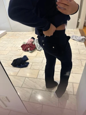 Mörkblå velourbyxor från Juicy Couture - Säljer ett par mörkblå velourbyxor från Juicy Couture med broderad logga på benet och fickor med knappar bak. Byxorna har bootcut-modell och är riktigt mjuka och sköna. Perfekta för en chill och trendig look.