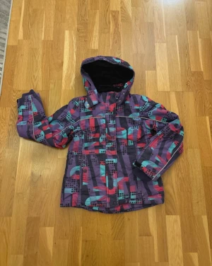 Mönstrad vinterjacka från Lindex - Vinterjacka från Lindex i storlek 146. Vadderad luva som går att ta av. Reflex baktill.