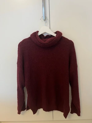 Vinröd polotröja från Ellos - Mysig vinröd polotröja från Ellos i stickat material. Tröjan har en hög, rullad polokrage och långa ärmar. Passformen är lite loose och perfekt för kyliga dagar. Enkel och stilren design som är lätt att matcha med jeans eller leggings.