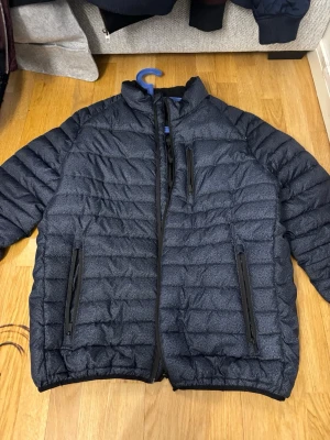 Svart pufferjacka från Bluewear XL - Säljer en svart pufferjacka från Bluewear i storlek XL. Jackan har quiltad design, tre dragkedjeförsedda fickor och hög krage. Materialet är syntet och polyester, perfekt för kalla dagar. Enkel och stilren look som funkar till det mesta.