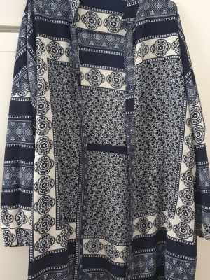 Klänning - Säljer en långklänning från Boohoo i marinblått och vitt med ett detaljerat mönster som påminner om paisley och blommor. Klänningen har långa ärmar och är tillverkad i ett mjukt, lätt material. Perfekt för dig som gillar boho-stil och snygga prints. Lite nopprig.