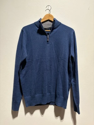 Blå half zip tröja från Occhi & Belli - Mörkblå långärmad tröja från Occhi & Belli med half zip och hög krage. Tröjan är i mjukt material och har ribbade muddar vid ärmslut och nederkant. Perfekt för lager på lager under kyliga dagar.