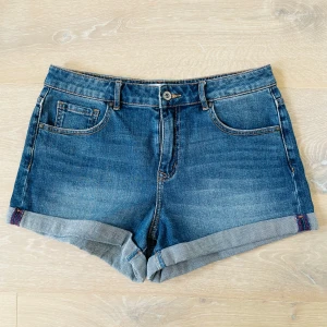 Blå jeansshorts med upprullad kant - Snygga blå jeansshorts med upprullad kant och klassiska fem fickor. Shortsen har normal passform och stängs med knapp och dragkedja. Perfekta för sommaren och enkla att matcha med olika toppar. Nästan oanvända – bara använda ett par gånger! 🩳 Inga skador, rena och i mycket fint skick. Säljer dem eftersom storleken inte längre passar.  Mått: • Midja: 80 cm • Höfter: 100 cm • Längd: 29 cm  📦 Kan hämtas i Kista, Stockholm, eller skickas