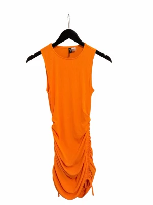 Orange ärmlös kortklänning med snörning - Säljer en snygg orange ärmlös klänning från DIVINED H&M. Klänningen är kort och har snörningsdetalj på sidan som ger en draperad effekt.