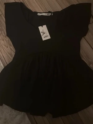 Svart blus med volang - Säljer en svart blus från lager157 i storlek XS. Blusen har korta ärmar, rund halsringning och en söt volang nedtill som ger en flowy känsla. Perfekt att styla med jeans eller kjol för en trendig look.