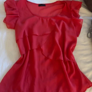 Ljus röd blus med volangdetaljer - Säljer en röd blus, lite korall färg nästan och är super fin på