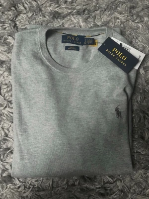 Polo Ralph Lauren stickad tröja - Snygg ljusgrå tröja från Polo Ralph Lauren i bomull. Merino ull tröja i slim fit. Storlek S. Den är helt ny med prislappen kvar på.
