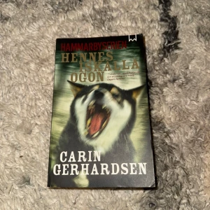Hennes iskalla ögon - En spännande bok ur Hammarbyserien som fångar dig direkt! Omslaget visar en ylande hund, vilket ger en mystisk och dramatisk känsla. Perfekt för dig som gillar nervkittlande berättelser och vill ha något riktigt svårt att lägga ifrån dig.