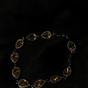 Silverfärgat armband med gula stenar - Snyggt armband med droppformade, facetterade gula stenar infattade i silverfärgad metall. Stenarna är omgivna av små glittriga detaljer som ger extra bling. Perfekt för dig som gillar att sticka ut med accessoarer som har lite lyxig känsla.