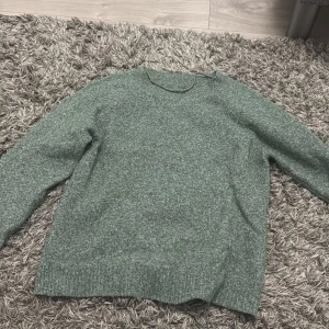 Grön stickad tröja med rund hals - Mysig grön stickad tröja med rund hals och långa ärmar. Tröjan har en enkel design med ribbade muddar vid ärmslut och nederkant, perfekt för att hålla värmen under kyliga dagar. Passar dig som gillar en chill och stilren look.