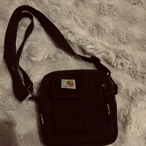 Svart axelväska från Carhartt - Snygg svart axelväska från Carhartt med justerbar rem och flera fack med dragkedja. I bra skick 