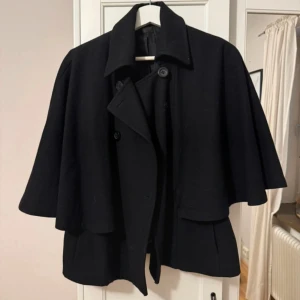 Poncho kappa - Säljer en svart poncho kappa med bred krage och dubbelknäppning framtill. Jackan har vida, trekvartsärmar och en snygg, lös passform. Perfekt för dig som vill ha en stilren och trendig look. Skriv vid frågor.💕skulle säga en storlek S/M. Tyvärr har en knapp ramlat av men som ni ser på bilderna är det inte anmärkningsvärt💗