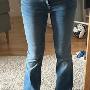 Blå bootcut jeans med låg midja - Snygga blå jeans med bootcut passform och låg midja. Jeansen har klassisk femficksdesign och är tillverkade i mjukt denimtyg. Färgen är mellanblå med lätt slitning framtill och baktill för en cool look.