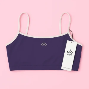 Lila linne från Alo Yoga - Säljer en snygg lila linne-topp från Alo Yoga med tunna axelband och vit kant runtom. Toppen har minimalistisk logga framtill och är gjord i ett stretchigt syntetmaterial som passar perfekt till träning eller yoga.