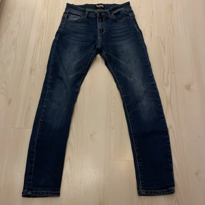 Blå skinny jeans från Denimway - Snygga blå jeans från Denimway i storlek 152. Modellen är skinny med smal passform och klassisk femficksdesign. Jeansen har coola slitningar och tvättade detaljer som ger en modern vibe. Perfekt för dig som gillar en inte för tajt look och streetstyle.