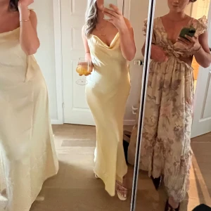 Ljusgul långklänning med blommiga axelband - Superfin ljusgul långklänning i satinliknande material med smickrande draperad urringning och axelband dekorerade med små blommor. Klänningen har en elegant, figurnära passform och faller snyggt längs kroppen. Perfekt för dig som vill sticka ut med en romantisk och trendig look.