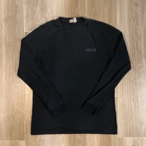 Svart långärmad tröja Posty Co. - Svart långärmad tröja från Posty Co. med diskret logga tryckt på bröstet. Tröjan har rund hals och är gjord i mjuk bomull, perfekt för dig som gillar enkel och clean stil. Passar dig som vill ha en basic men snygg tröja.
