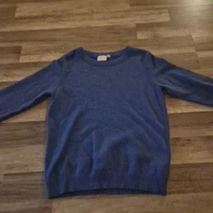 Blå stickad tröja från Vila - Blå stickad tröja från Vila med rund hals och ribbade muddar vid ärmslut och nederkant. Tröjan har en enkel och klassisk design med långärmade ärmar, perfekt för att hålla dig varm under kyliga dagar. Passar dig som gillar stilrena och bekväma plagg.