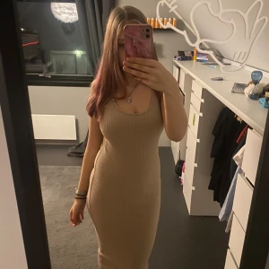 Beige ribbad långklänning - Säljer en beige ribbad långklänning med rundad halsringning och ärmlös design. Klänningen har en tight passform som framhäver figuren och är tillverkad i ett stretchigt material som sitter skönt mot kroppen. Perfekt för dig som gillar stilrena och enkla plagg.