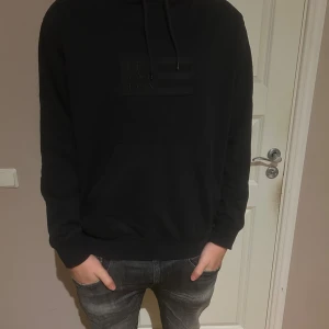 Svart hoodie från Lexington - Svart hoodie från Lexington med broderad logga på bröstet. Klassisk känguruficka framtill, dragsko i huvan och mjukt material. Perfekt för dig som gillar en clean och stilren look.