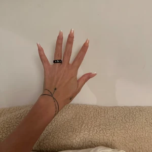 Svart ring med stenar från Multi Collection - Snygg svart ring från Multi Collection med tre glittrande stenar infällda runt om. Ringen har en bred och stilren design som ger en cool vibe. Perfekt för dig som gillar att sticka ut med dina accessoarer.