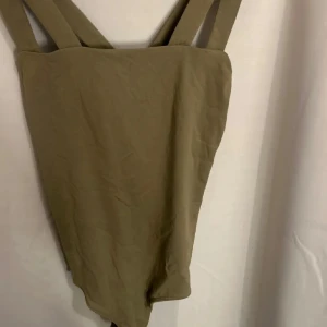 Olivgrön body från BikBok XS - Snygg olivgrön body från BikBok i storlek XS. Modellen har breda axelband som korsas i ryggen och en enkel, stilren design utan mönster. Materialet känns mjukt och stretchigt, perfekt för strandhäng eller poolparty.