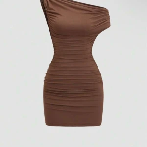 Brun one shoulder kortklänning - Snygg brun kortklänning med one shoulder-design och rynkade detaljer längs hela klänningen. Figurnära passform som framhäver siluetten. Tillverkad i mjukt och stretchigt material för en bekväm känsla.  Säljer då jag då den aldrig kommit till användinf