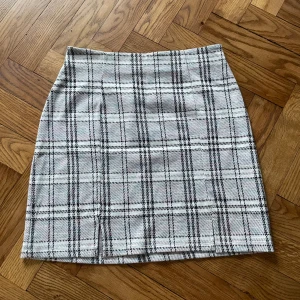 Rutig kortkjol från Lindex - Snygg rutig kortkjol från Lindex i storlek 158/164. Kjolen har ett klassiskt rutmönster i vitt, grått och svarta toner med inslag av rosa och blått. Rak passform och mjukt syntetmaterial som är bekvämt att bära. Perfekt för dig som gillar preppy stil.