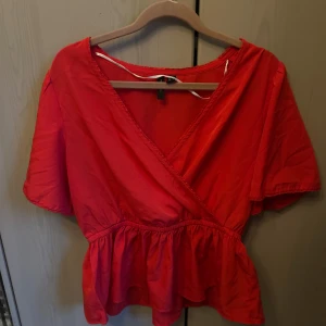 Röd omlottblus - Säljer nu denna röda omlottblus från Vero Moda i storlek XS. Blusen har korta ärmar, v-ringad omlottfront och volang nedtill🤩 Har endast använt den enstaka gånger så är som ny! Pris går att diskutera 💕