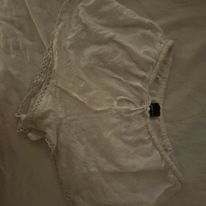 Vita broderade shorts från Gina Tricot - Vita shorts från Gina Tricot i storlek S. De har broderade blommor, snörning i midjan och fina spetsdetaljer längs kanterna. Loose passform med mjukt bomullsmaterial. Använda en gång.