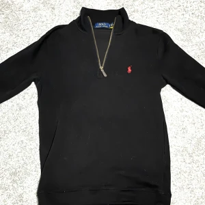 Svart Polo Ralph Lauren Half Zip  - Säljer en svart långärmad tröja från Polo Ralph Lauren i storlek S med klassisk röd logga broderad på bröstet. Tröjan har en half zip-dragkedja och hög krage, perfekt för lager-på-lager. Tillverkad i mjuk bomull för en skön känsla.