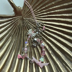 Hello Kitty-inspirerat rosa armband - Supergulligt phone string med Hello Kitty-berlock, pärlor i rosa och vitt, små hjärtan, stjärnor och rosetter. Phone stringen har flera söta detaljer som en rosa rosett och glittriga pärlor, perfekt för dig som älskar kawaii-stil och pastellfärger.