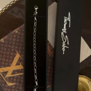 Thomas Sabo silver charm-armband - Stilrent charm-armband från Thomas Sabo i äkta silver. Armbandet har klassiska ovala länkar och en rund bricka med ingraverad text 'CHARM CLUB THOMAS SABO'. Perfekt för att hänga på dina favoritberlocker och skapa en personlig look. 20 cm långt. Material: 925 Sterlingsilver. Modell: charm armband classic short. Ordpris: 1099kr