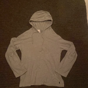 Grå hoodie från Polo Ralph Lauren - Snygg grå hoodie från Polo Ralph Lauren med klassisk huva och snörning. Tröjan har lång ärm och är tillverkad i mjuk bomull. Diskret Polo-logga broderad i mörkblått vid nederkanten. Perfekt för chill dagar och enkel att matcha med jeans eller joggers. Den är mindre än vad man tror och passar perfekt på mig som är 178 så passar i de som söker storlek M
