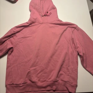 Rosa hoodie med huva och snörning från lager 157 - Säljer en rosa hoodie med huva och snörning. Tröjan har långa ärmar och ribbade muddar vid nederkant och ärmslut. Perfekt för chill dagar och enkel att matcha med jeans eller mjukisbyxor. Materialet känns mjukt och bekvämt mot huden.