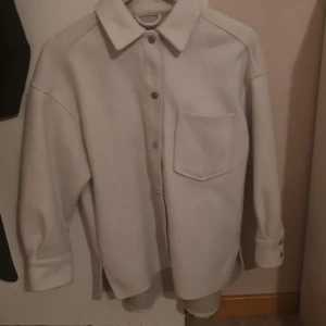 Overshirt i ull från Zara, XS - Snygg overshirt från Zara i ljusbeige ullmix. Modellen har klassisk krage, stora silvriga knappar framtill och på ärmsluten, samt en bröstficka. Passformen är loose och den har längre baksida för extra cool look.